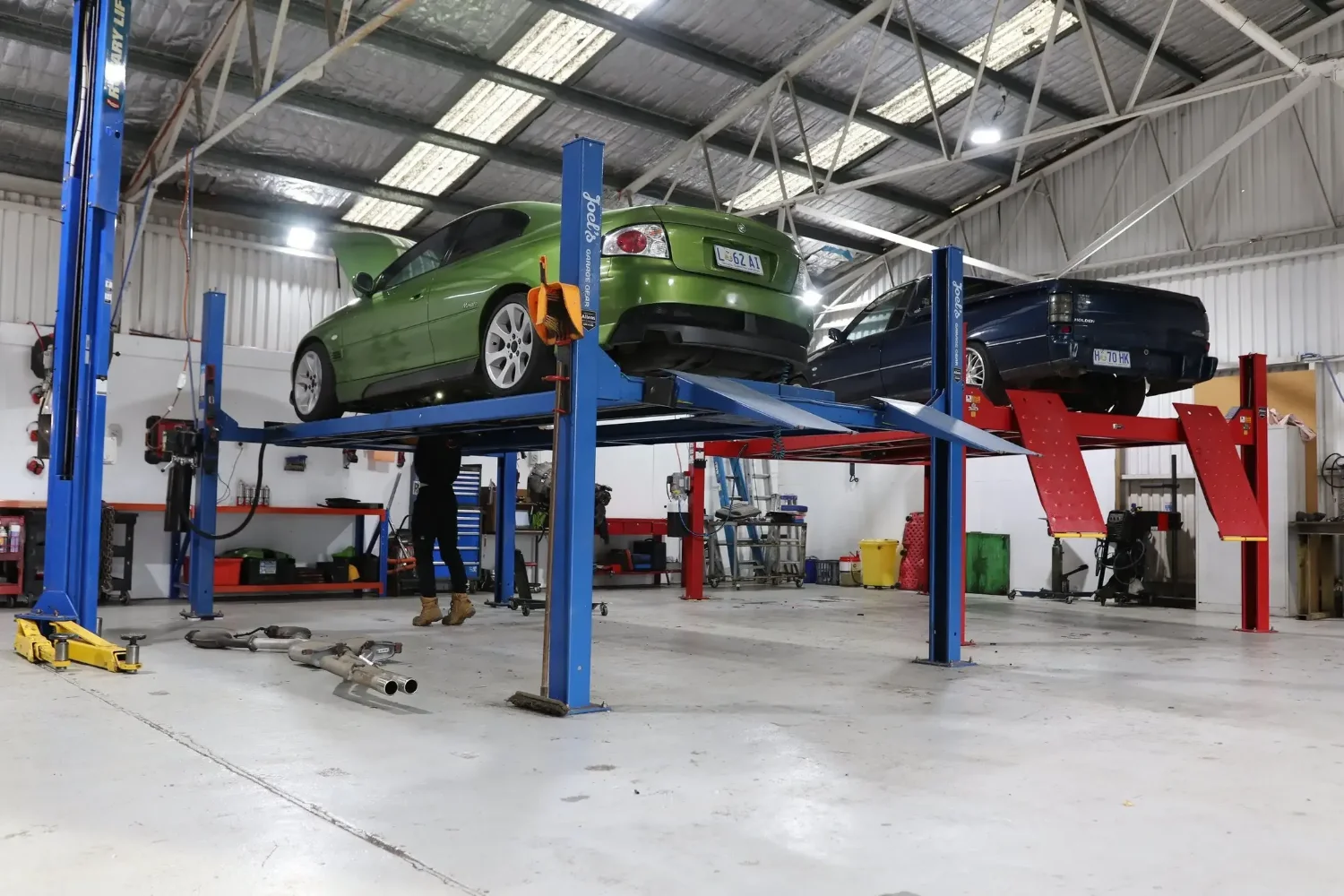 Two classic Australian vehicles on hoists inside the Launceston Motorworks workshop